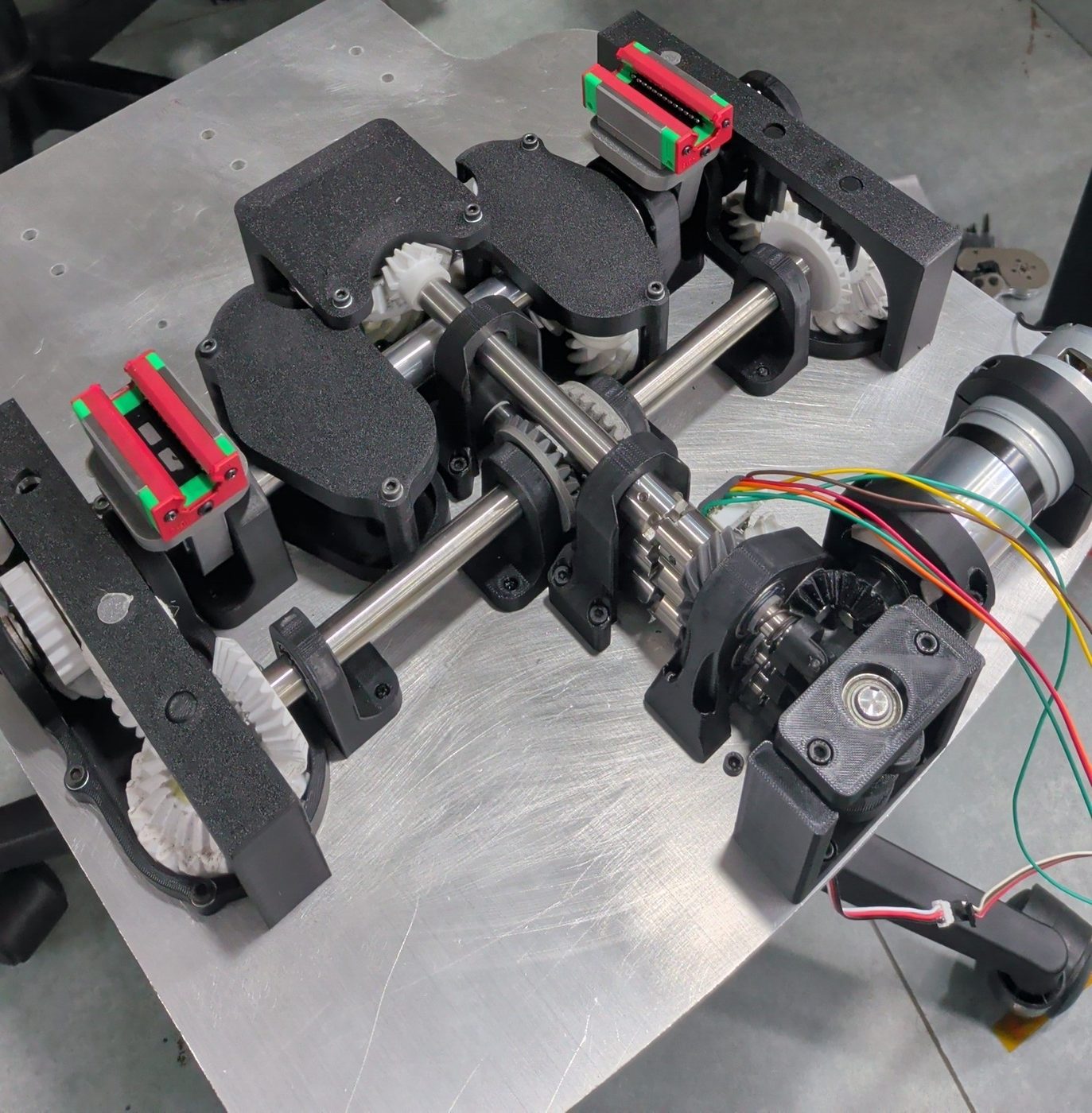 Early Flow transmission prototype: bevel and spur gearing on ground shafts between printed housings, with linear rails and a DC motor at right.